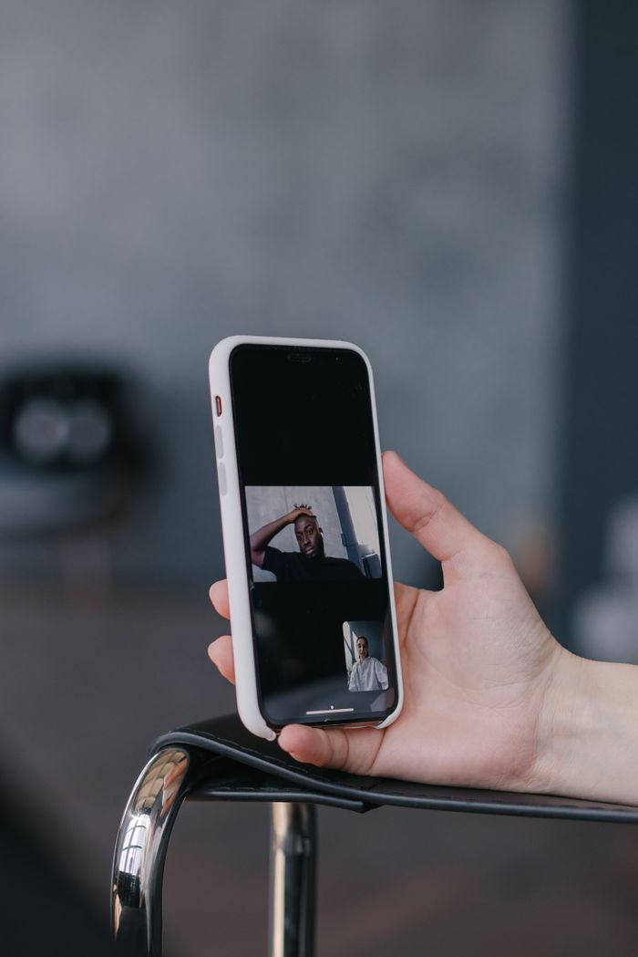 Close-up of a hand holding a smartphone displaying a video call with a blurred background.